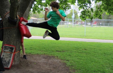 Teenage boy kicking bag on tree.